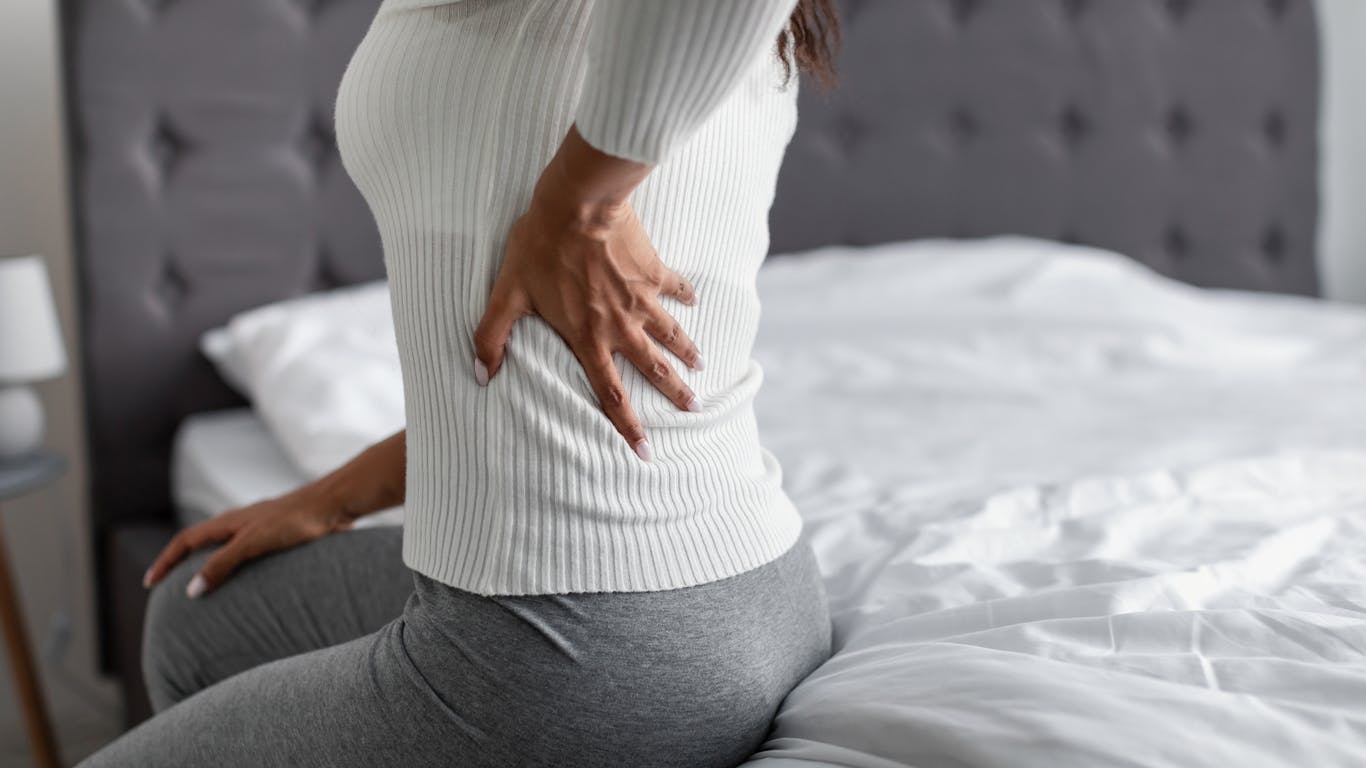 woman sitting up in bed experiencing back pain stock photo